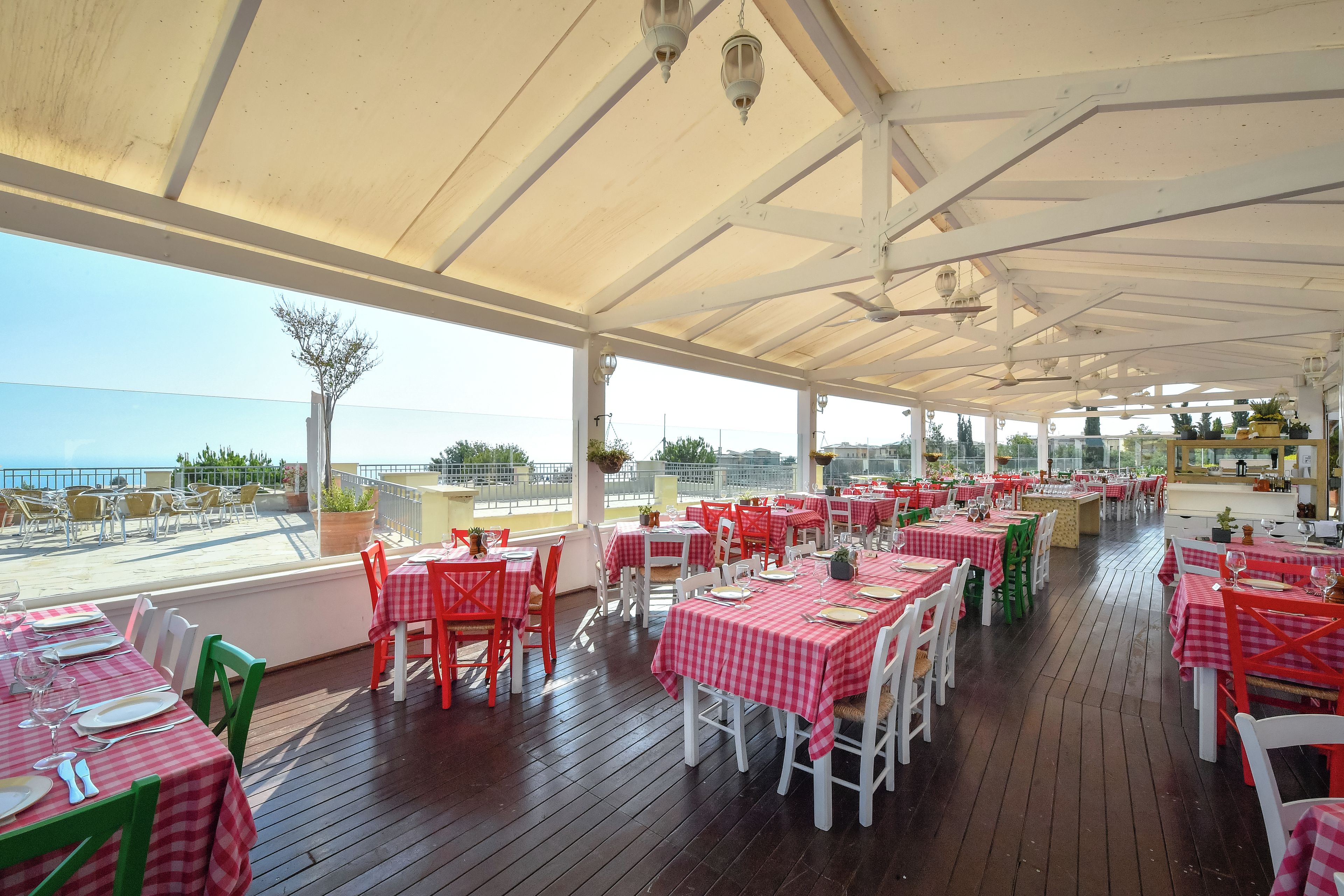 Een openluchtrestaurant met tafels en stoelen, een houten terras en uitzicht op zee.