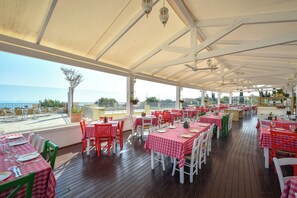 An outdoor restaurant with tables and chairs, a wooden deck, and a view of the sea. - Aphrodite Hills Residences Superior Villas (Kouklia)