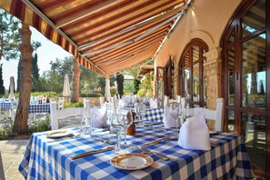 Een terras met een geruit tafelkleed, witte stoelen en servies, klaar voor een maaltijd.
