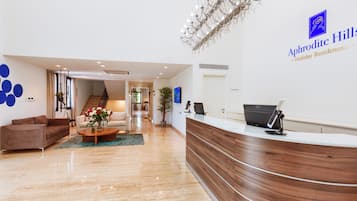 A reception area with a wooden reception desk, a chandelier, and a sign for 'Aphrodite Hills Holiday Residences.'