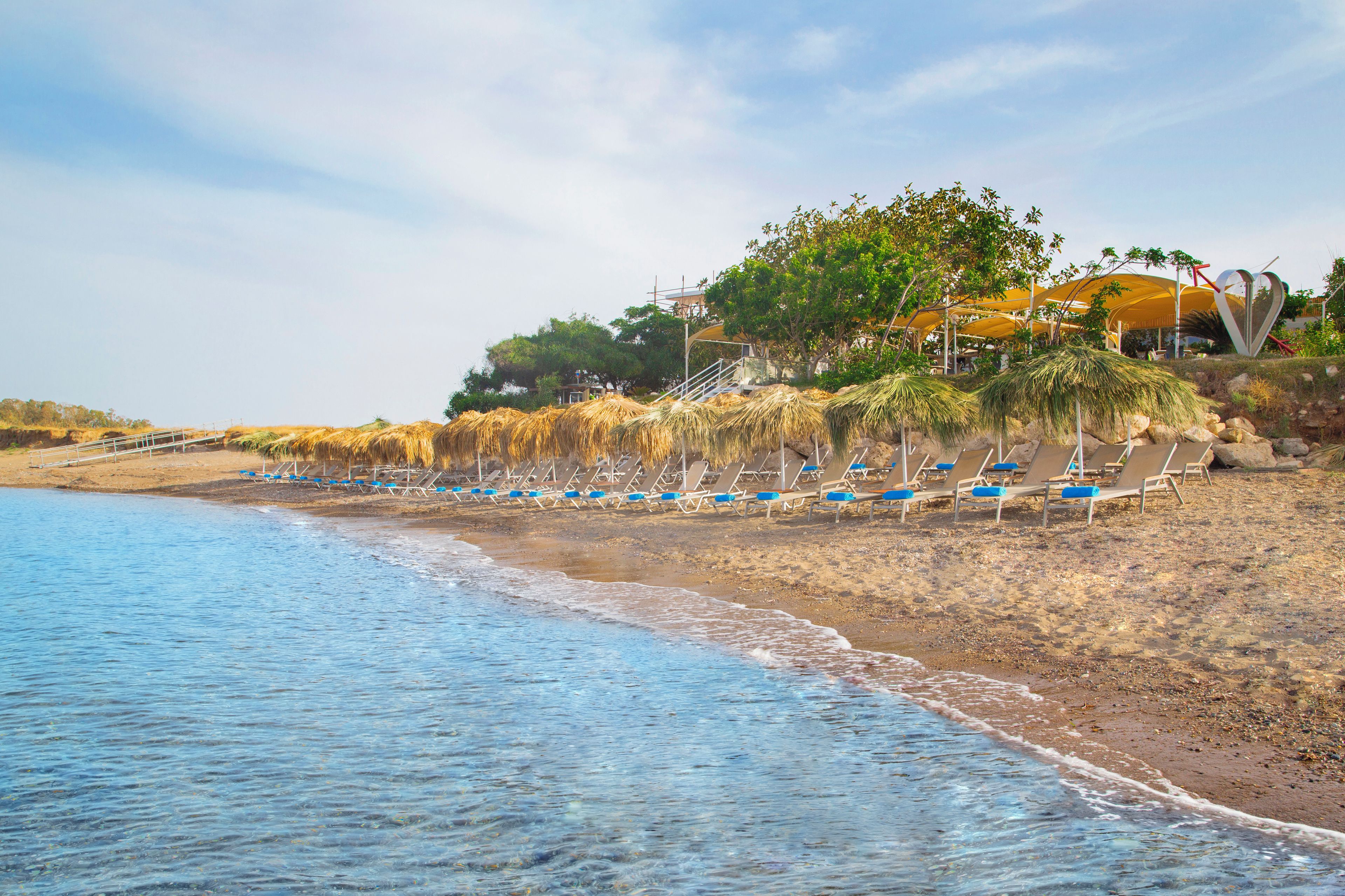 Une plage bordée de rangées de chaises longues, avec un bâtiment au toit jaune en arrière-plan.