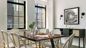 A dining area with a dark wooden table, white wicker chairs, and a black cabinet with a framed abstract artwork. - Boulevard Stays Downtown Nashville (Nashville)