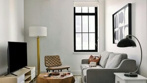 A living room with a flat-screen TV, a round coffee table, a sofa, a chair, a floor lamp, and a window with blinds. - Boulevard Stays Downtown Nashville (Nashville)