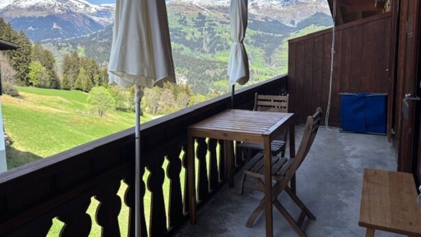 Ein Balkon mit Tisch und Stühlen, Blick auf eine Berglandschaft und ein rustikales Holzhäuschen im Inneren.