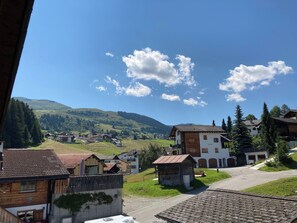 Ein Dorf mit traditionellen Holzhäusern, einem zentralen Gebäude mit einem Schild und einem klaren, blauen Himmel.