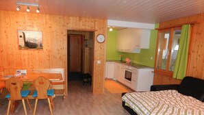 Ett rum med en säng, ett skrivbord med stolar, en köksdel och en dörr som leder till ett annat rum.