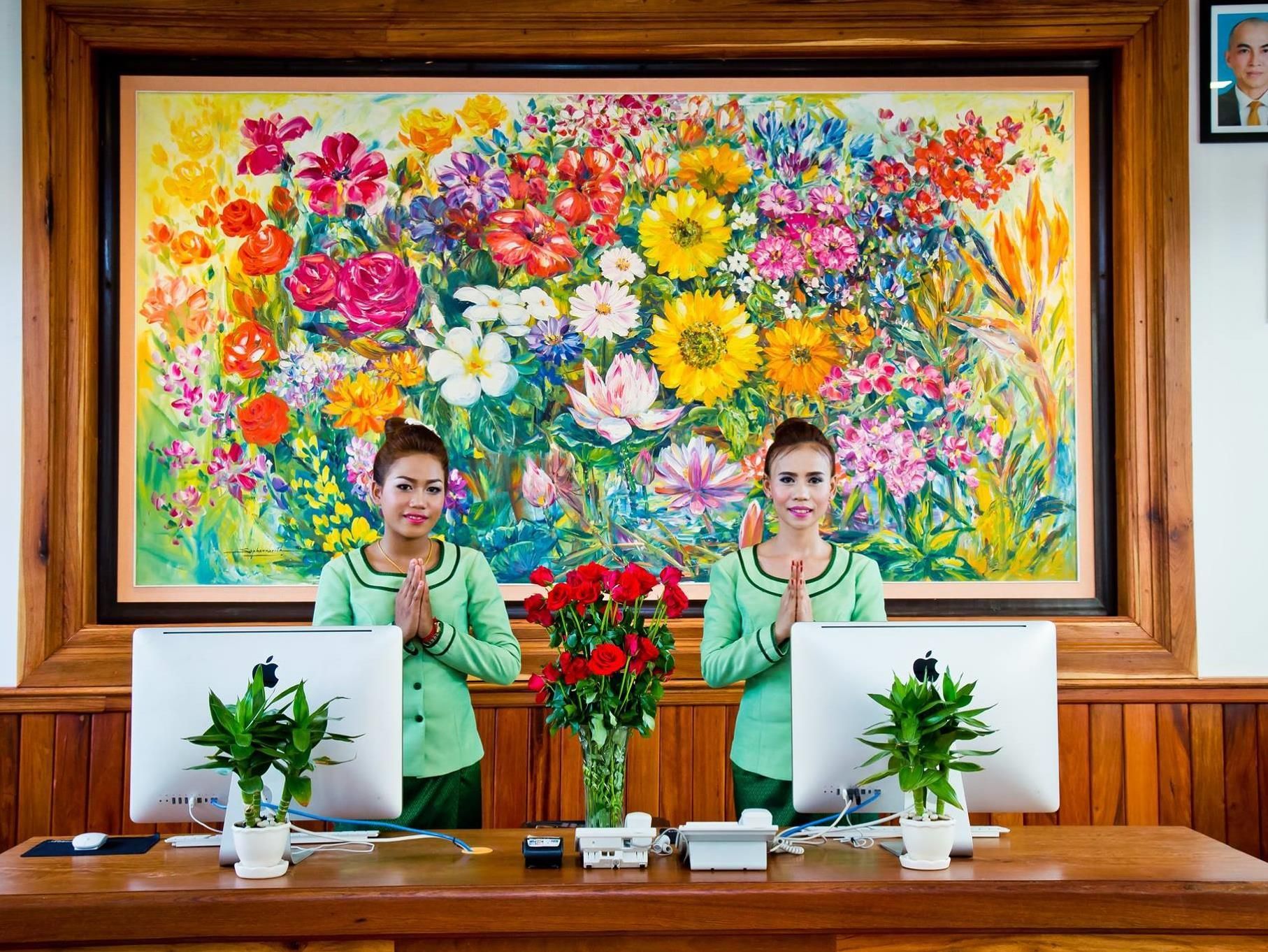 Zwei Personen sitzen an einem Schreibtisch mit Apple Computern, einem Blumenbild und Topfpflanzen.