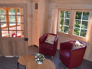 A wooden interior with two red leather chairs, a small round table with a floral centerpiece, and large windows with a view of greenery. - Gyrgarta, Obersaxen-Meierhof, (Obersaxen), 34066B by Interhome (Obersaxen Affeier)