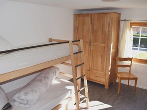 A bunk bed with a ladder, a wooden wardrobe, a chair, and a window with curtains. - Gyrgarta, Obersaxen-Meierhof, (Obersaxen). by Interhome (Obersaxen Affeier)
