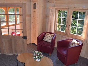 A wooden room with two red leather chairs, a wooden table, and a window with a view of greenery. - Gyrgarta, Obersaxen-Meierhof, (Obersaxen). by Interhome (Obersaxen Affeier)