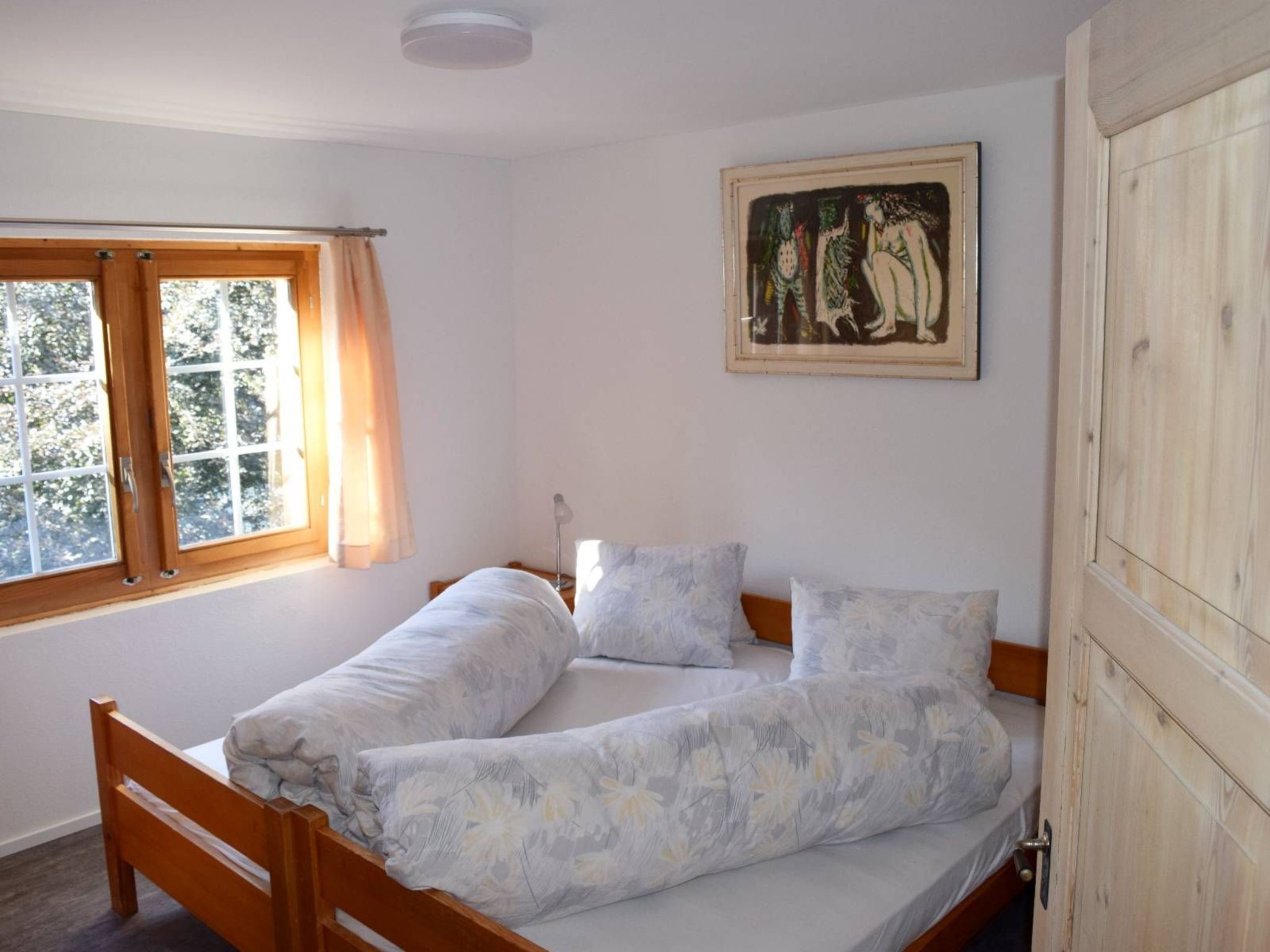 A bedroom with a wooden bed, a window with curtains, and a painting on the wall.