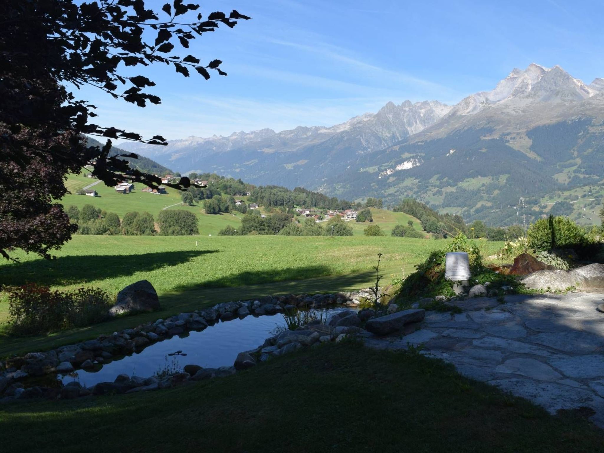 Ländliche Landschaft mit einem kleinen Teich, einem Steinweg und Häusern im Tal.