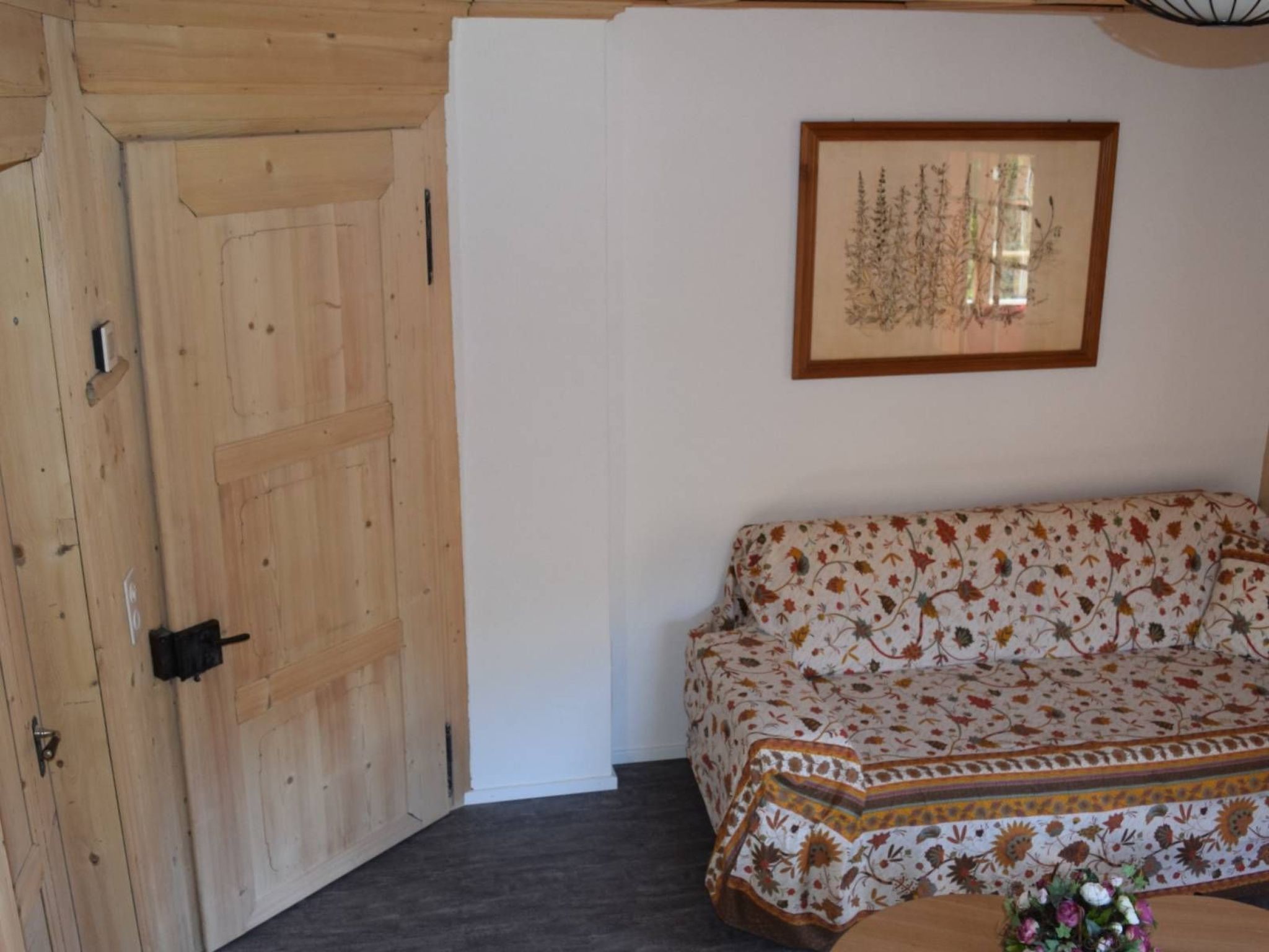 A room with a wooden door, a patterned sofa, and a framed artwork on the wall.