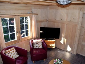 A wooden-paneled room with two leather chairs, a television, and a window with curtains. - Gyrgarta, Obersaxen-Meierhof, (Obersaxen). by Interhome (Obersaxen Affeier)