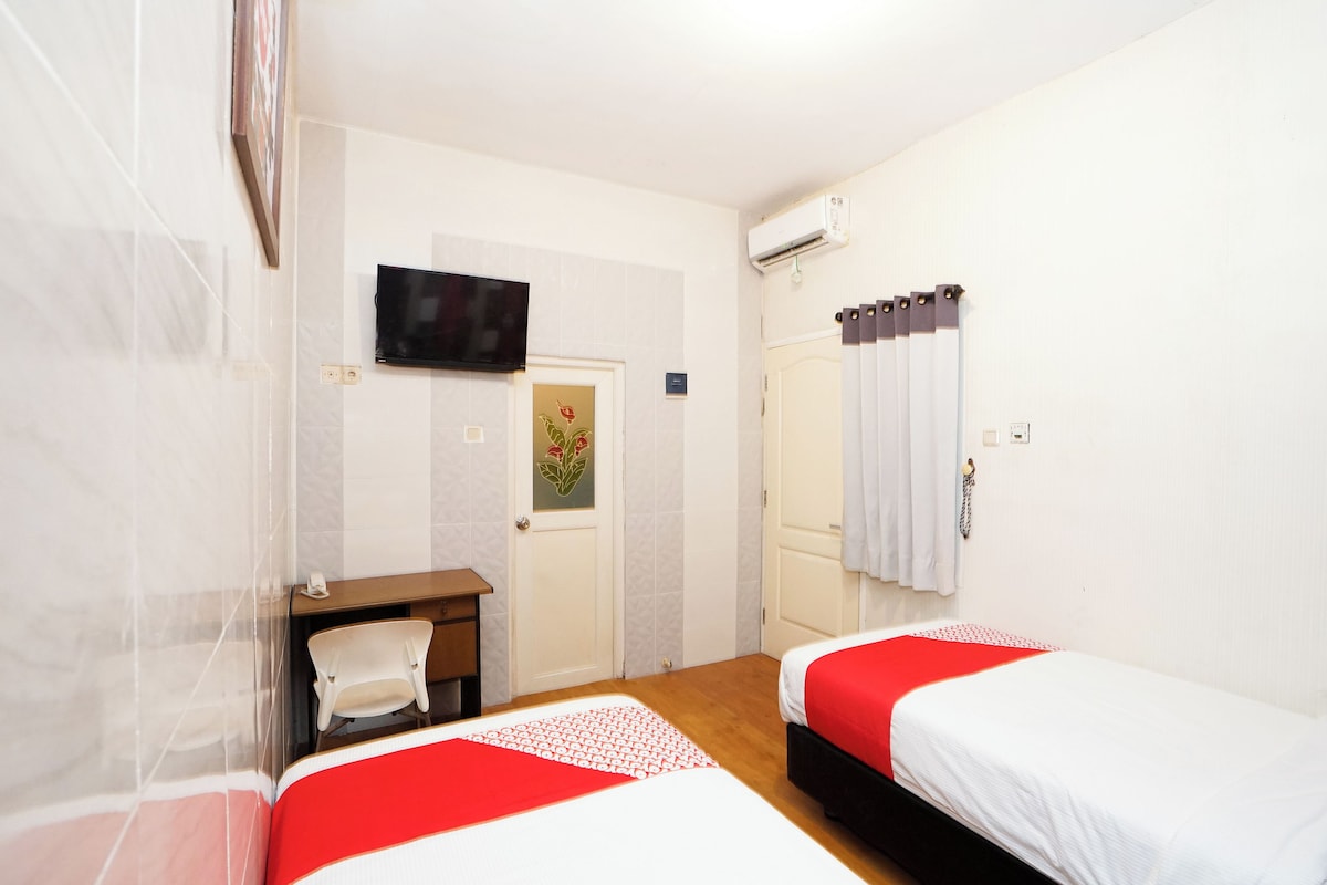 Ein Hotelzimmer mit zwei Betten, einem Fernseher, einem Schreibtisch und einer Tür mit einem Blumenbild.