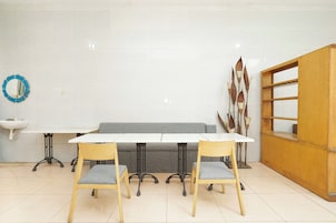 Un comedor con mesa blanca, dos sillas de madera, un sofá gris, un mueble de madera y un adorno azul en la pared.