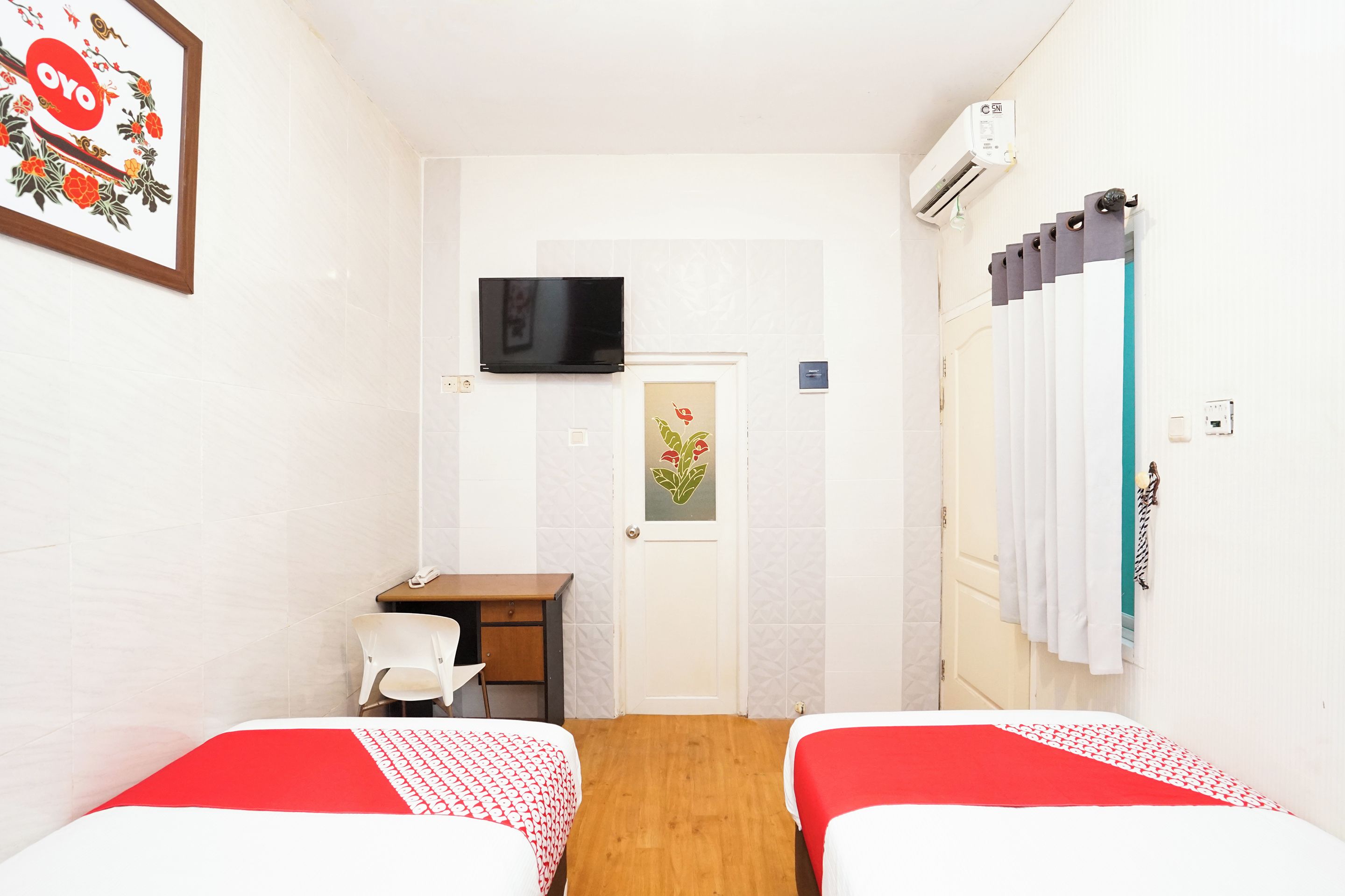 A hotel room with two beds, a desk, a chair, a TV, and a door with a floral decoration.