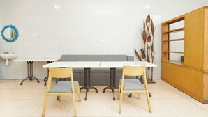A dining area with a white table, two wooden chairs, a grey sofa, a wooden cabinet, and a blue decorative item on the wall. - OYO 425 Mojokerto Guesthouse (Mojokerto)
