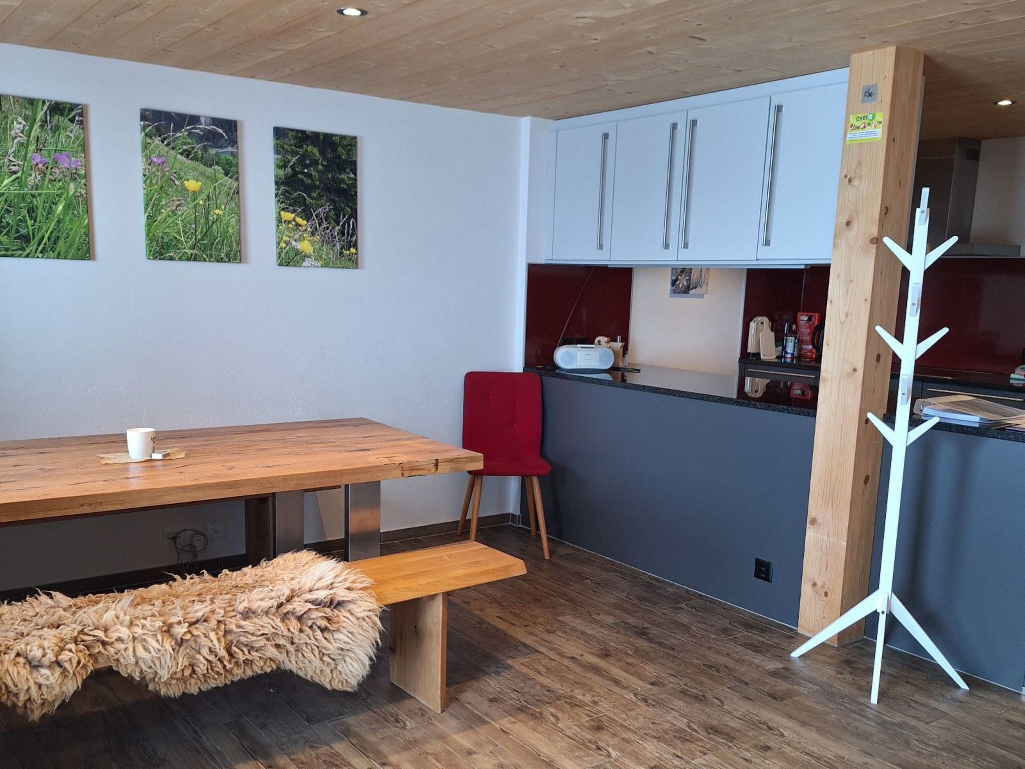 Een moderne keuken met witte kasten, een houten eettafel, een rode stoel en een pluizig vloerkleed.