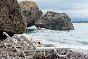 Une plage avec des chaises longues et une table où sont disposés de la nourriture et des boissons, le tout avec vue sur l’océan.