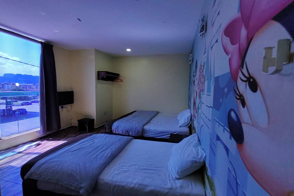 A hotel room with two beds, a window with a view of a cityscape, a wall with a cartoon character mural, and a mounted TV.