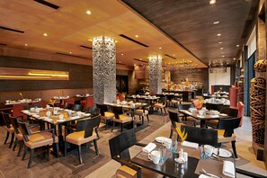 A restaurant with multiple dining tables and chairs, decorative pillars, and a modern ceiling design.