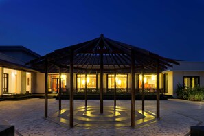 Um gazebo com piso circular, um edifício com grandes janelas e uma entrada bem iluminada.