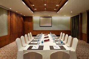 A conference room with a long table, chairs, water bottles, and a projector screen. - Radisson Blu Resort & Spa Alibaug (Alibag)
