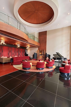A spacious lobby with a grand piano, red seating, and a high ceiling with a circular design. - Radisson Blu Resort & Spa Alibaug (Alibag)