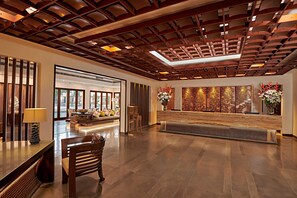 A spacious lobby with a wooden ceiling, a reception desk, seating area, and a large window.