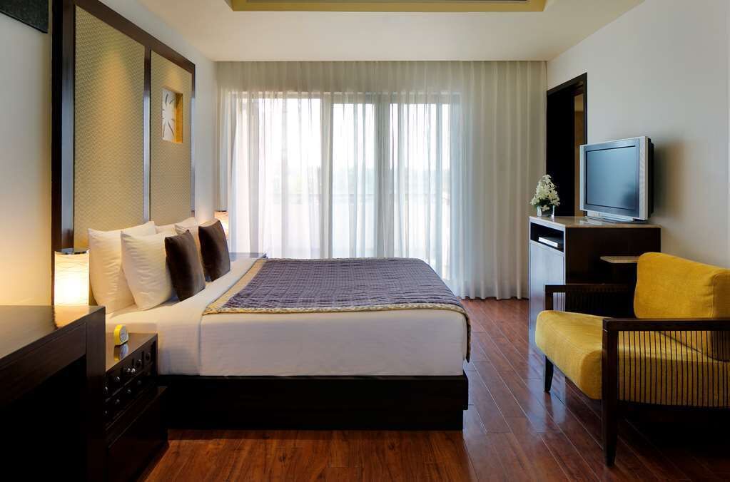 Una habitación de hotel con una cama, televisión, una silla y un escritorio.