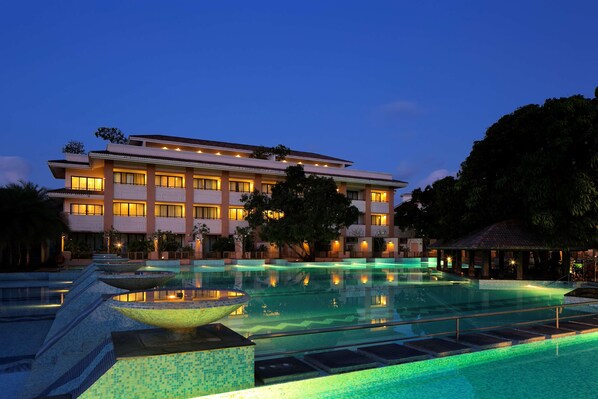 A hotel with a large swimming pool, multiple balconies, and a well-lit facade.