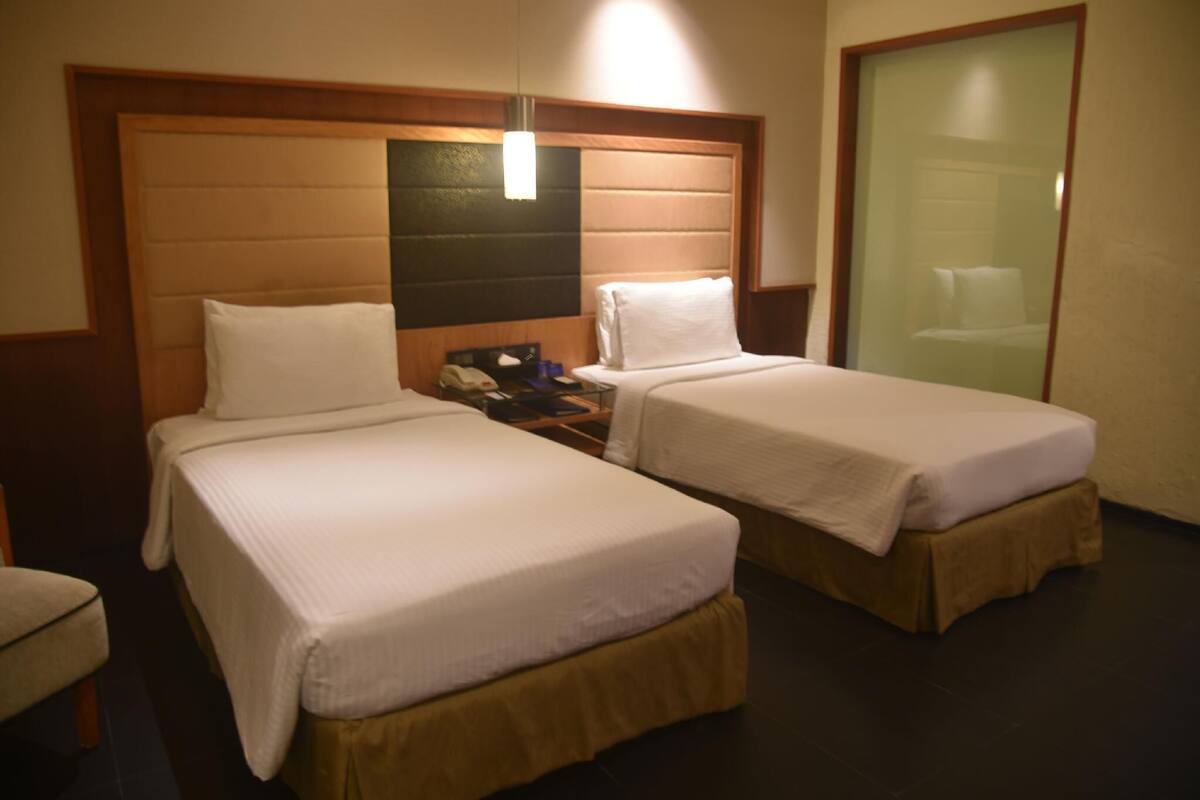 A hotel room with two single beds, a wooden headboard, a bedside table with a phone, and a glass door leading to a bathroom.
