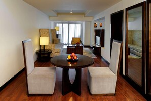 A hotel room with a round dining table, two armchairs, a sofa, a TV, and a large window with curtains. - Radisson Blu Resort & Spa Alibaug (Alibag)