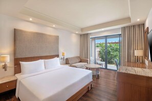 A hotel room with a large bed, a sofa, a small table, a desk, and a TV.