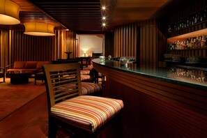 A bar area with wooden paneling, a counter with bottles, and striped cushioned chairs.