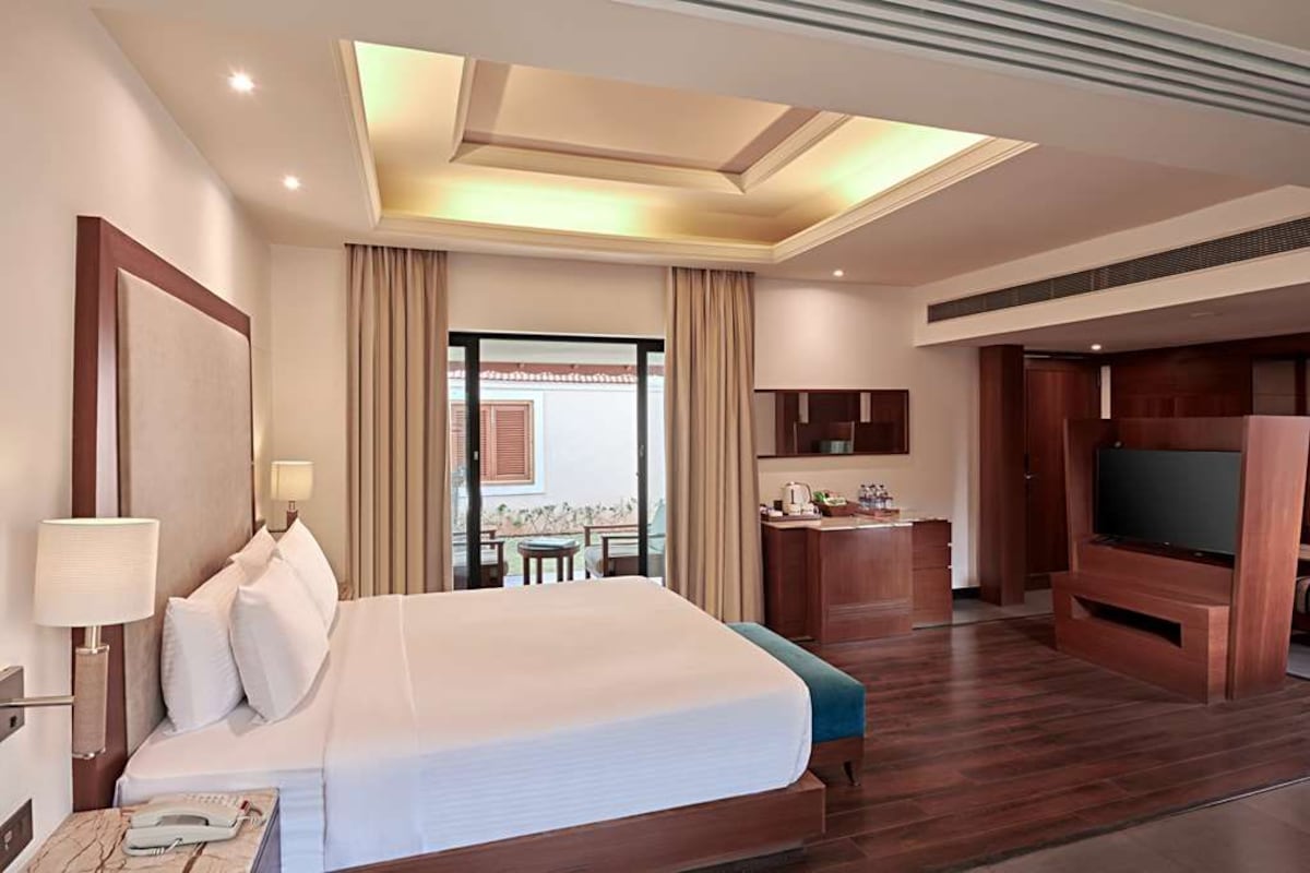 Habitación de hotel con una cama grande, un escritorio, un televisor y un balcón con cortinas.