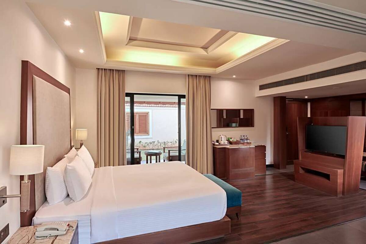 A hotel room with a large bed, a desk, a TV, and a balcony with curtains.