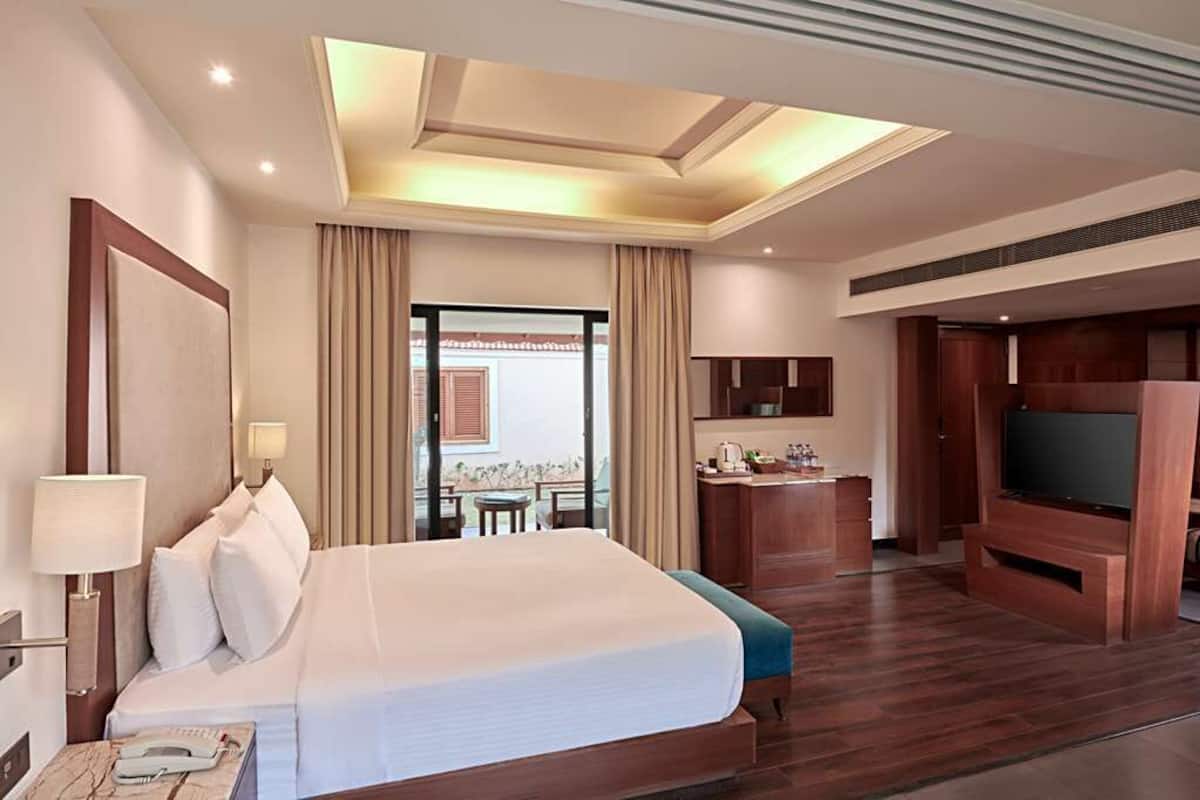 Habitación de hotel con una cama grande, un escritorio, un televisor y un balcón con cortinas.