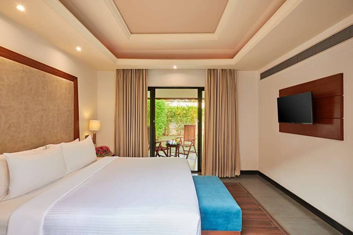 A hotel room with a large bed, a TV mounted on the wall, and a view of the outdoors through a glass door.