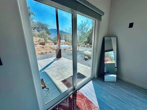 Quarto com uma grande porta de vidro deslizante que dá para um alpendre externo com piso de pedra e vista para uma paisagem montanhosa.