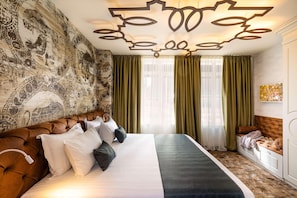 Habitación de hotel con una cama grande, cortinas verdes, un papel tapiz estampado y una lámpara en el techo.