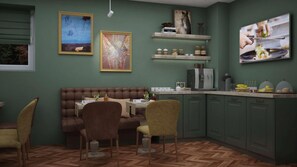 A dining area with a brown sofa, two chairs, a table, and a kitchen with green cabinets and a coffee machine.