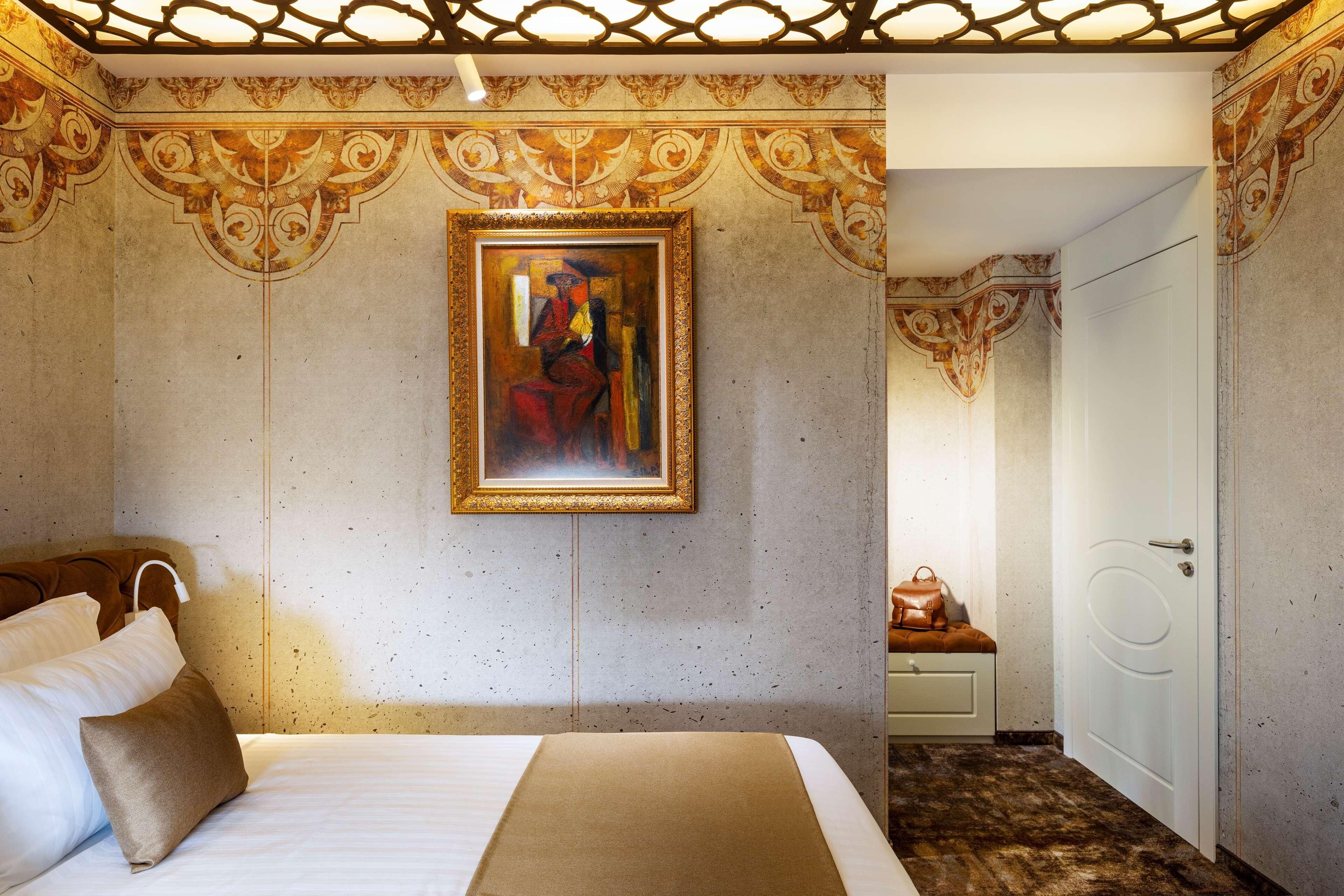 A hotel room with a bed, a painting on the wall, and a door leading to another room.