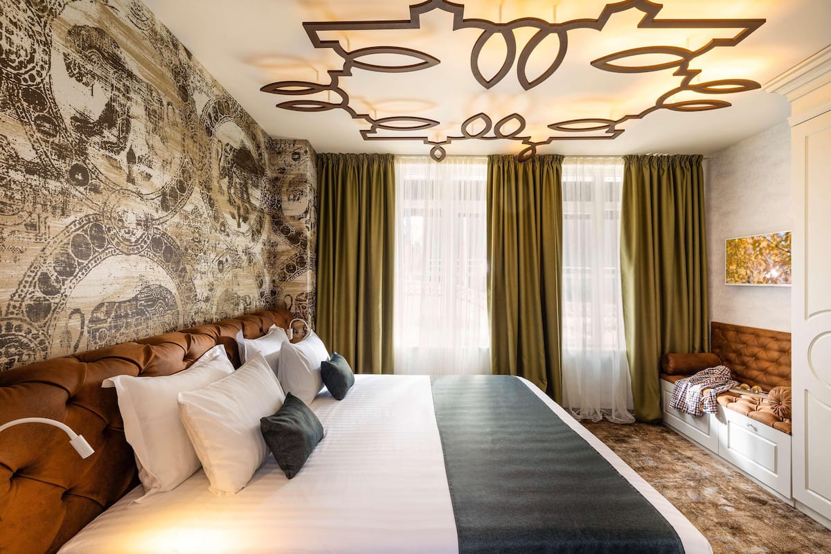A hotel room with a large bed, green curtains, a patterned wall, and a ceiling light fixture.