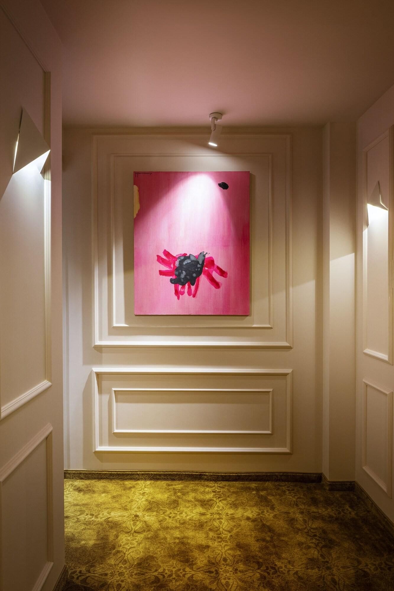 A hallway with a pink artwork, a patterned carpet, and a white door.