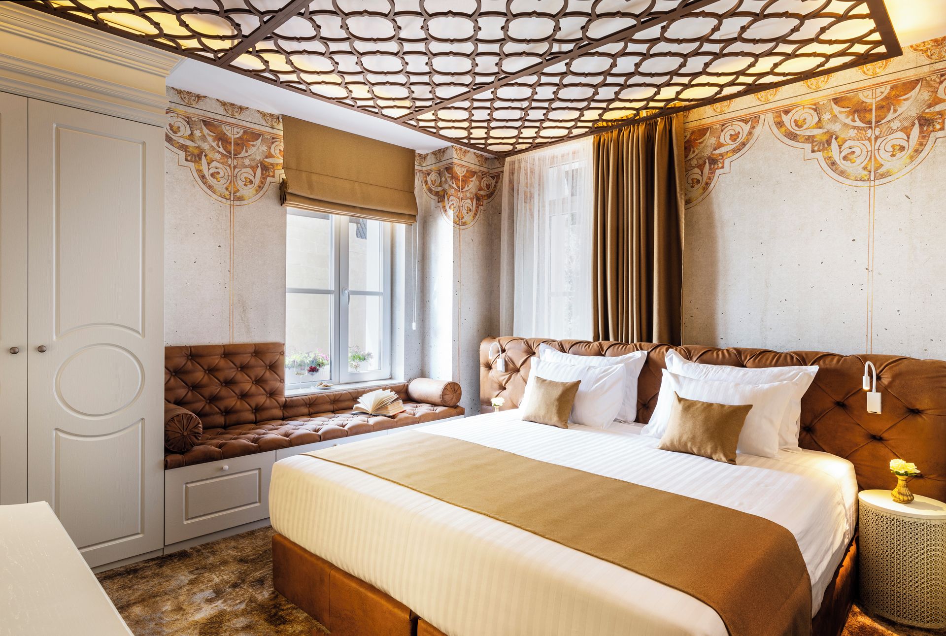 Quarto com uma cama grande, área de estar com um banco acolchoado, guarda-roupa e teto decorativo.