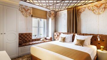 Quarto com uma cama grande, área de estar com um banco acolchoado, guarda-roupa e teto decorativo.