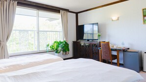 Habitación de hotel con dos camas, un escritorio con televisor, una silla y una planta en maceta.