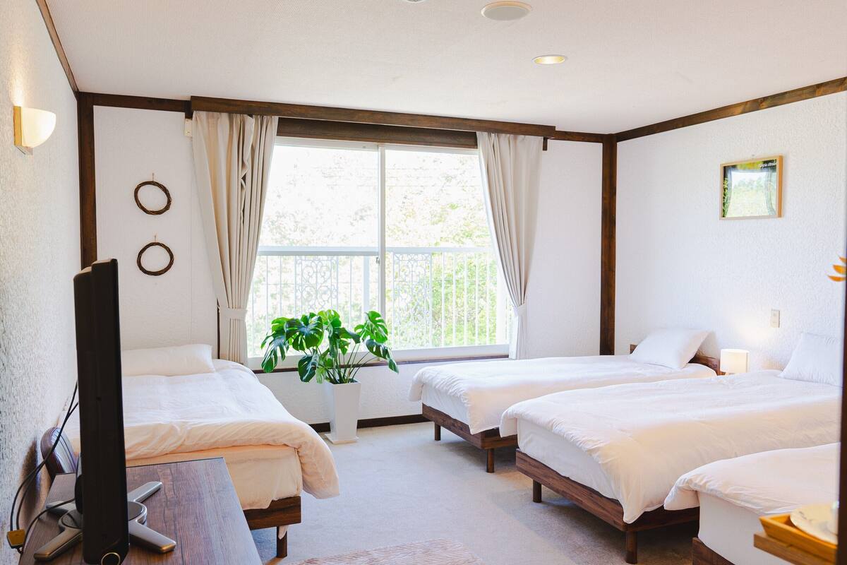 Une chambre d’hôtel avec deux lits, un bureau avec un ordinateur, une plante en pot et une fenêtre avec des rideaux.